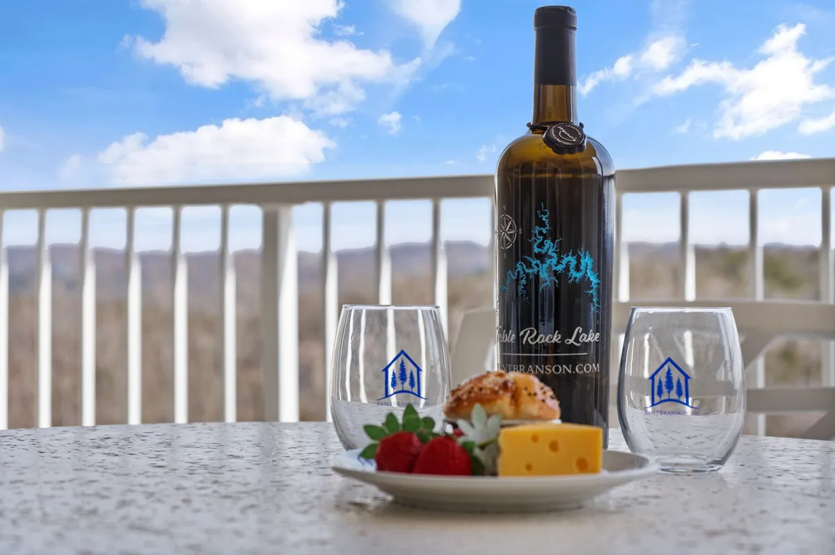 This image presents an outdoor setting with a wine bottle, cheese platter, strawberries, and glasses arranged on a table, set against a scenic backdrop. The mood is casual yet refined, capturing the essence of outdoor dining and the pleasure of savoring local flavors while enjoying the view.