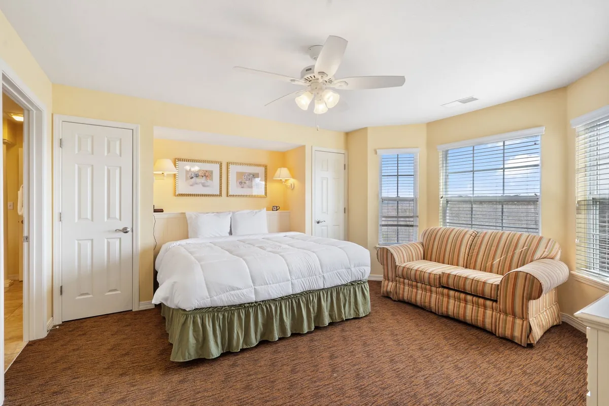 A cozy king bedroom with a plush bed, striped couch, and large windows allowing natural light to fill the space. The room exudes comfort and is ideal for relaxing or enjoying a quiet morning.