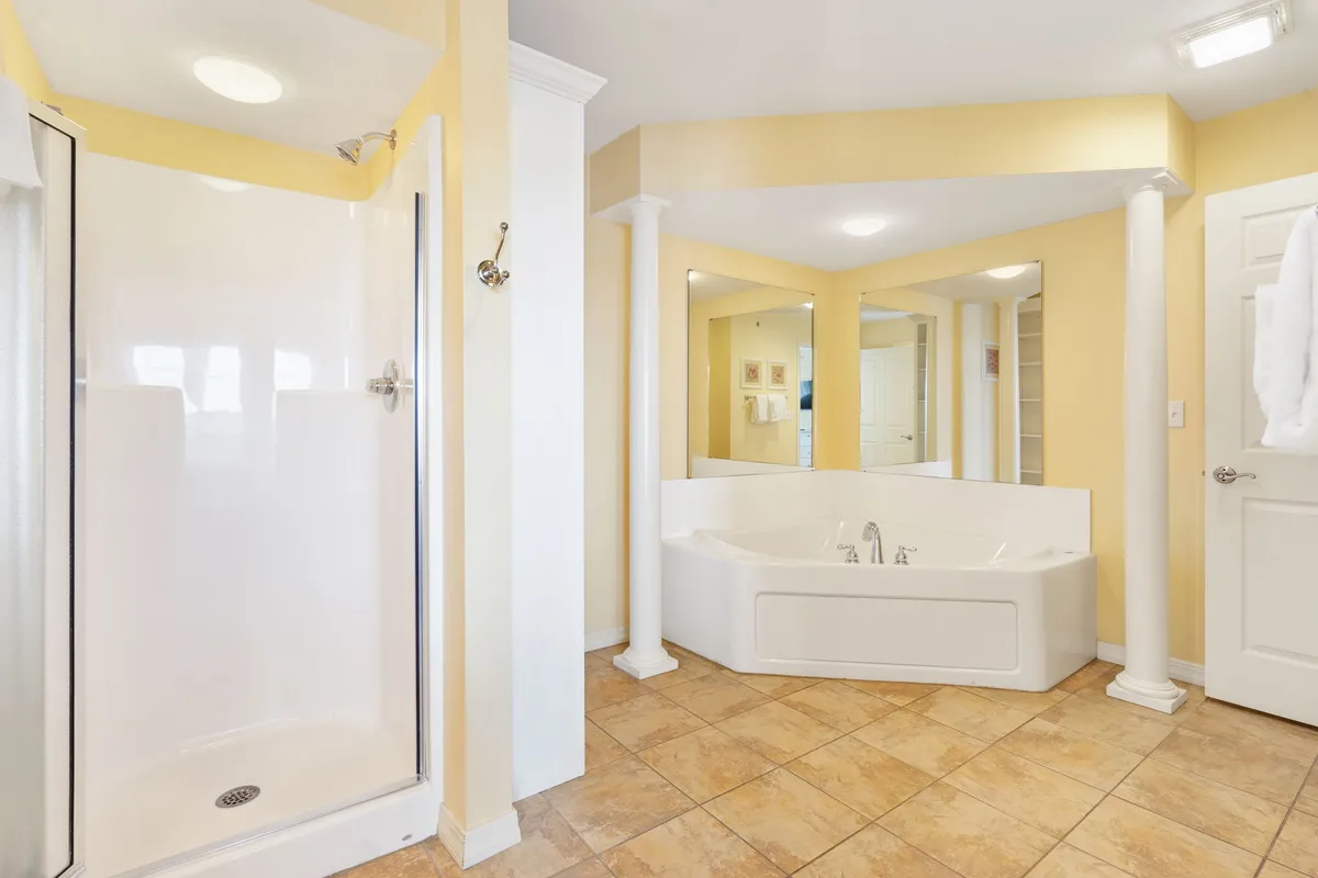 A tranquil bathroom with a large soaker tub, separate shower area, expansive mirror, and decorative pillars. The serene atmosphere is conducive to relaxation and self-care.