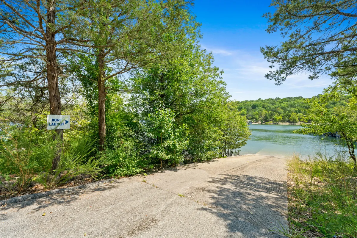 A close-up exterior view of a boat launch area, prominently displaying a boat launch sign, a tranquil lakefront, and rich surrounding trees. The view suggests easy, immediate water entry and the possibility for fishing or launching a boat, perfectly matching the section’s focus on water-based pursuits.