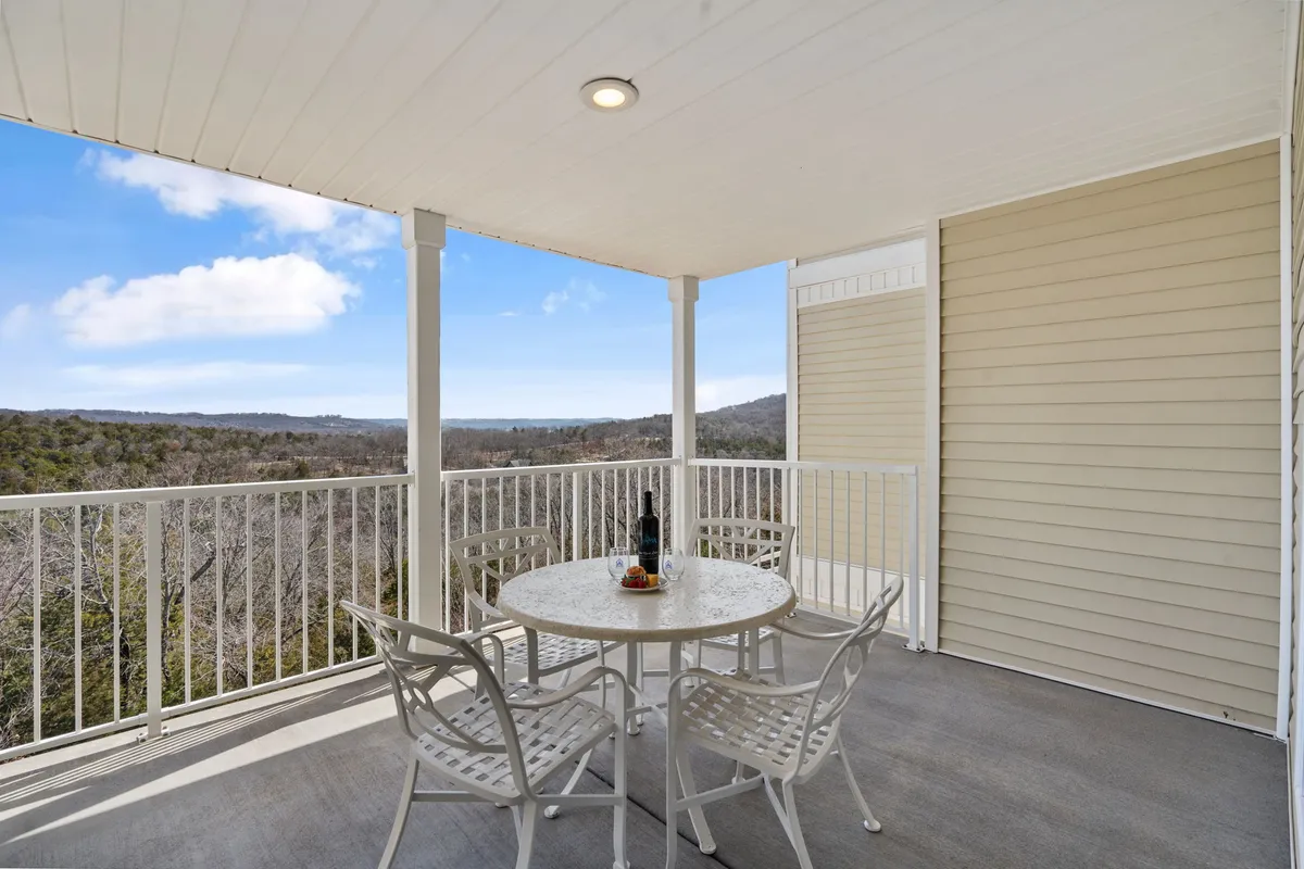 This image captures an inviting outdoor deck area with a table and chairs set for relaxation. A bottle of wine and a fruit platter rest on the table as the deck opens to a sweeping landscape view, suggesting a perfect spot for al fresco meals or drinks at sunset. The seating arrangement is comfortable, and the peaceful outdoor atmosphere is ideal for unwinding.