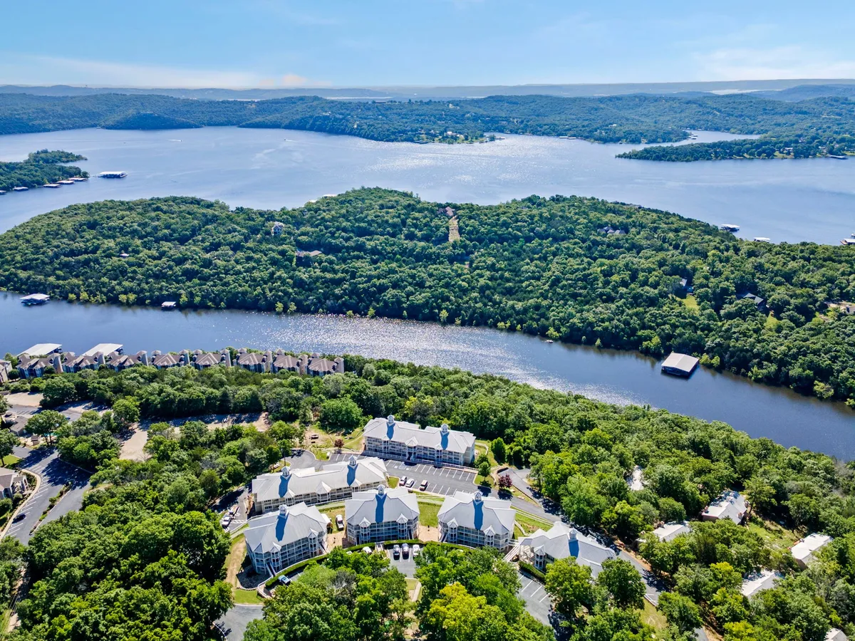 This image features a tranquil lakeside setting with calm water, surrounding hills, residential buildings, and accessible roadways. The open, natural space suggests ample opportunity for outdoor activities such as hiking and picnicking with pets.