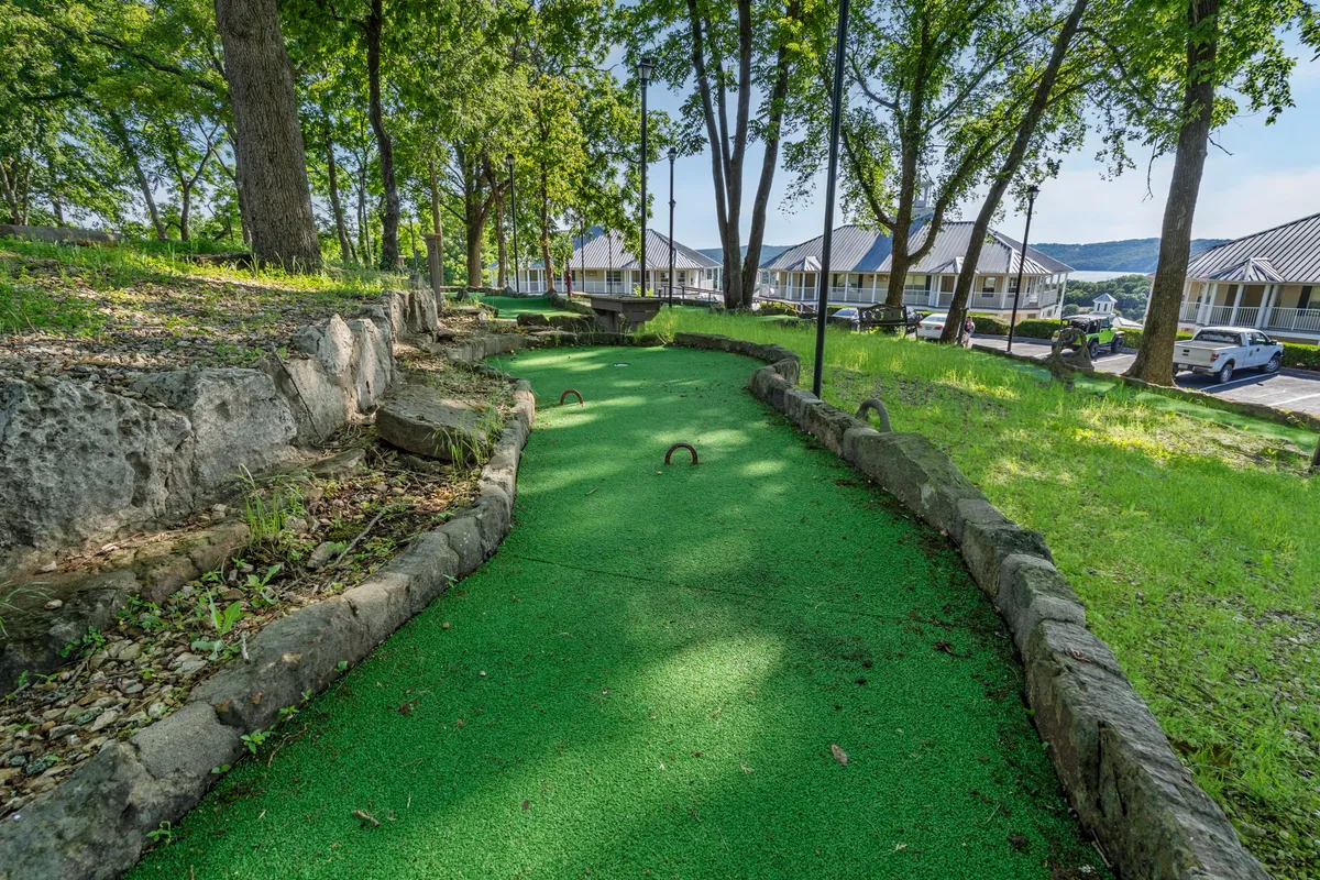 A lively exterior image showcasing a mini-golf course with natural stone borders and lush green trees overhead, creating a welcoming spot for picnicking, friendly competitions, and relaxing family time.