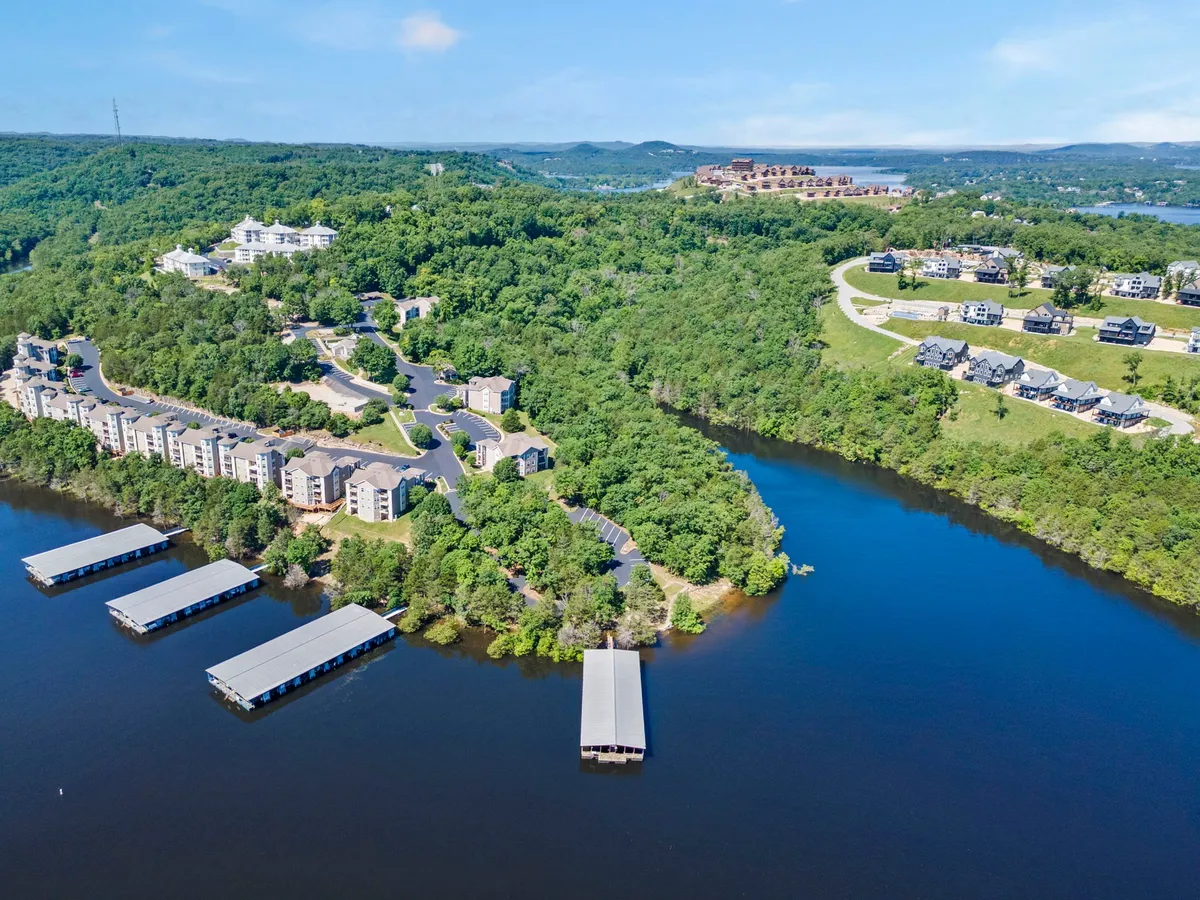 A picturesque view of waterfront properties, marina docks, lush greenery, and hillside homes. The expansive outdoor space highlights the beauty and variety of the Ozarks environment, suitable for strolls and nature walks with pets.
